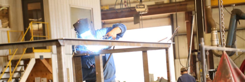 Factory worker carefully welding near a dust collector