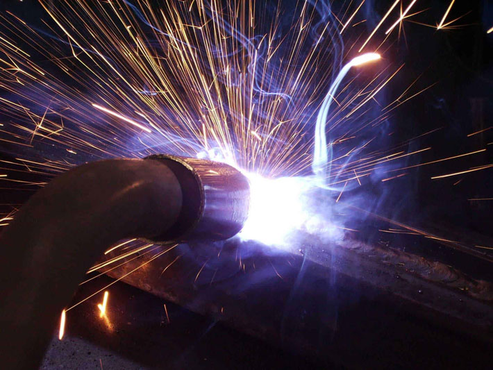 Closeup of welding gun creating sparks and fumes in a robotic weld cell